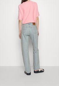 Camisa de manga corta rosa claro combinada con pantalones vaqueros de pierna ancha azul claro. Los pantalones cuentan con bolsillos traseros y una etiqueta de cuero marrón en la cintura.