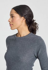 Pulover gri cu dungi, cu decolteu rotund, design ajustat și textură moale; modelul are părul închis la culoare aranjat într-un coc lejer.