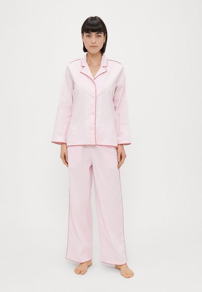 Conjunto de pijama que incluye una camisa de botones de manga larga y pantalones sueltos. Hecho de una suave tela rosa con detalles de ribete rojo en contraste.