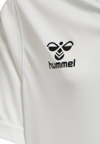 Hvid sports skjorte lavet af glat stof med et sort Hummel-logo og et strømlinet, minimalistisk design med korte ærmer.