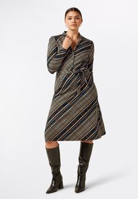 Tryckt omslagsklänning med marinblå bas och diagonala flerfärgade ränder, långa ärmar och midja med bälte; matchas med knähöga svarta stövlar.