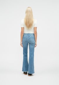 Lichtblauwe, hooggesneden flared jeans met achterzakken, gedragen met een nauwsluitend wit topje, met een gladde textuur en een casual ontwerp.