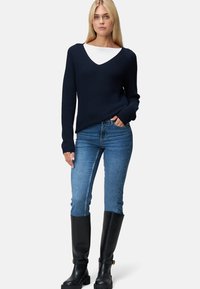 Pull en tricot bleu marine avec un col en V, associé à un jean en denim bleu clair et des bottes en cuir noir jusqu'aux genoux. Texture lisse et design ajusté.