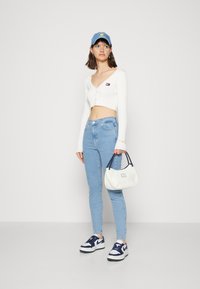 Suéter corto blanco acanalado con escote en V y cierre de botón, jeans de talle alto azul claro, bolso blanco con acentos en azul marino y zapatillas.