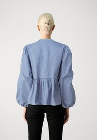 Μπλε και λευκή ριγέ μπλούζα με φουσκωτά μανίκια, συγκεντρωμένη μέση και στρογγυλή λαιμόκοψη. Φτιαγμένη από ελαφρύ ύφασμα, με διακριτική υφή.