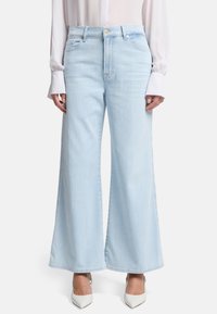 Jeans a gamba larga di un blu chiaro, realizzati in denim, con vita alta, tasche frontali e orlo pulito. Abbinati a scarpe con tacco alto bianche.