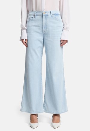 Jean large bleu clair en denim, avec une taille haute, des poches avant et un ourlet net. Associé à des chaussures à talons blancs.