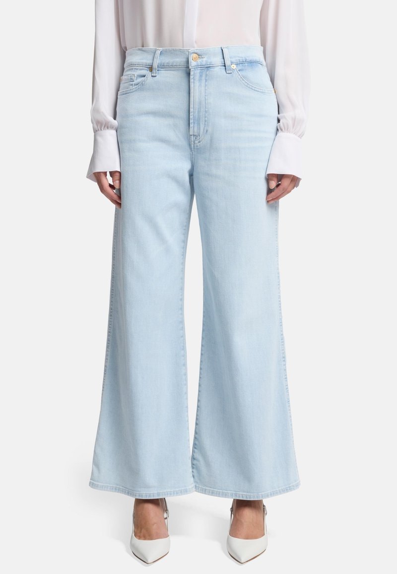 Jeans a gamba larga di un blu chiaro, realizzati in denim, con vita alta, tasche frontali e orlo pulito. Abbinati a scarpe con tacco alto bianche.