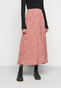 Red floral maxi skirt with a gathered waist, featuring small white flowers, buttons down the front, and paired with black lace-up boots.