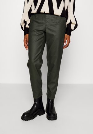 Persona con pantalones de cuero verde oscuro, botas negras gruesas y un jersey de patrón zigzag en negro y blanco.