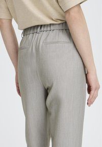 Světle šedé kalhoty na míru s hladkou texturou, vybavené elastickým pasem a dvěma zadními kapsami. Design je jednoduchý a elegantní.