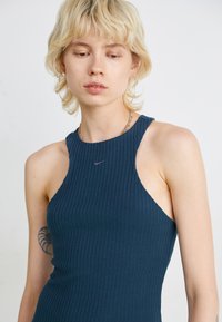 Jūrinės spalvos juostelė su aukštu kaklu ir šoninėmis išpjovomis. Puošia mažas purpurinis Nike logotipas. Lygus tekstūra, prigludęs dizainas.