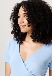 Light blue ribbed wrap top with short sleeves, featuring a deep V-neckline and smooth texture.