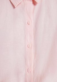 Pink linen shirt featuring a button-up front with six matching buttons and a pointed collar. Texture appears lightweight and soft.