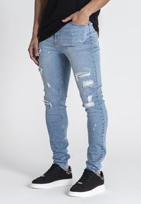 Ljusblå skinny jeans med slitna hål och färgsplatter, matchade med svarta sneakers med vit sula.