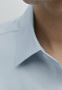 Camicia celeste con colletto, caratterizzata da una texture liscia del tessuto, chiusura con bottoni e bordi del colletto definiti, che evidenziano un design pulito e moderno.