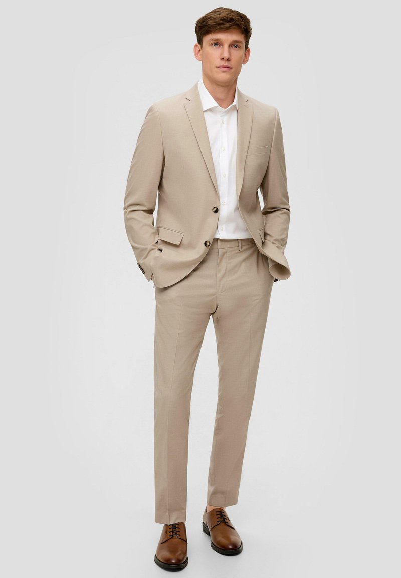 Beige Anzug mit einem einreihigen Sakko und geraden Hosen, kombiniert mit einem weißen Hemd und braunen Lederschuhen.