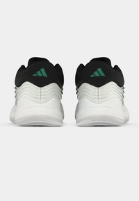 Par bijelih i crnih sportskih tenisica s zelenim trokutastim logom, prikazanih sa stražnje strane na ravnoj pozadini.