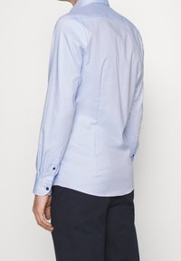 Light blue long-sleeve shirt in a smooth fabric, featuring a standard collar and buttoned cuffs, with subtle texture and fitted design.