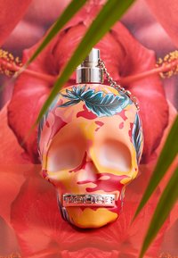 Transparent flasket i form av ett skull med en livlig orange och rosa camouflage-mönster, prydd med blå växtlighet och en silverkedja.