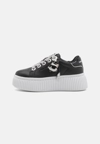 Sneaker nere in pelle con una spessa suola piattaforma bianca, caratterizzate da accenti argentati, lacci decorativi e un charm a forma di gatto.