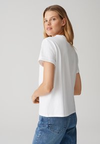 T-shirt bianco in cotone con maniche corte arrotolate, vestibilità comoda e orlo dritto. Indossato con jeans in denim blu, caratterizzati da sottili dettagli di cucitura.