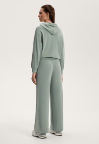 Világoszöld szabadidőruha kapucnival, széles szárú nadrággal. Puha tapintás, laza fazon és kiemelő varrások az oldalán.