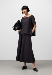 Czarny, teksturowany dwuczęściowy zestaw, składający się z bluzki z kwadratowym dekoltem i zwiewnej spódnicy, w połączeniu z czarnymi butami na slip-on oraz dużą torebką.