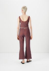 Stickad tvådelad outfit i blå och orange vågmönster; ärmlös crop top och utsvängda byxor med elastiskt midjeband; platta sandaler.