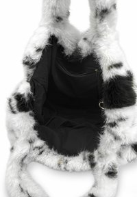Sac en fausse fourrure avec un extérieur tacheté noir et blanc, texture douce, et intérieur en tissu noir avec une poche zippée.