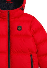 Giacca puffer rossa con zip frontale, cappuccio e accessori neri. Presenta una texture trapuntata e una piccola patch con logo sul lato sinistro del petto.