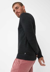 Donkergrijze gebreide trui met lange mouwen, geribbelde manchetten en een zijlabel. Gekleed met lichtroze corduroy broek, wat een casual uitstraling geeft.