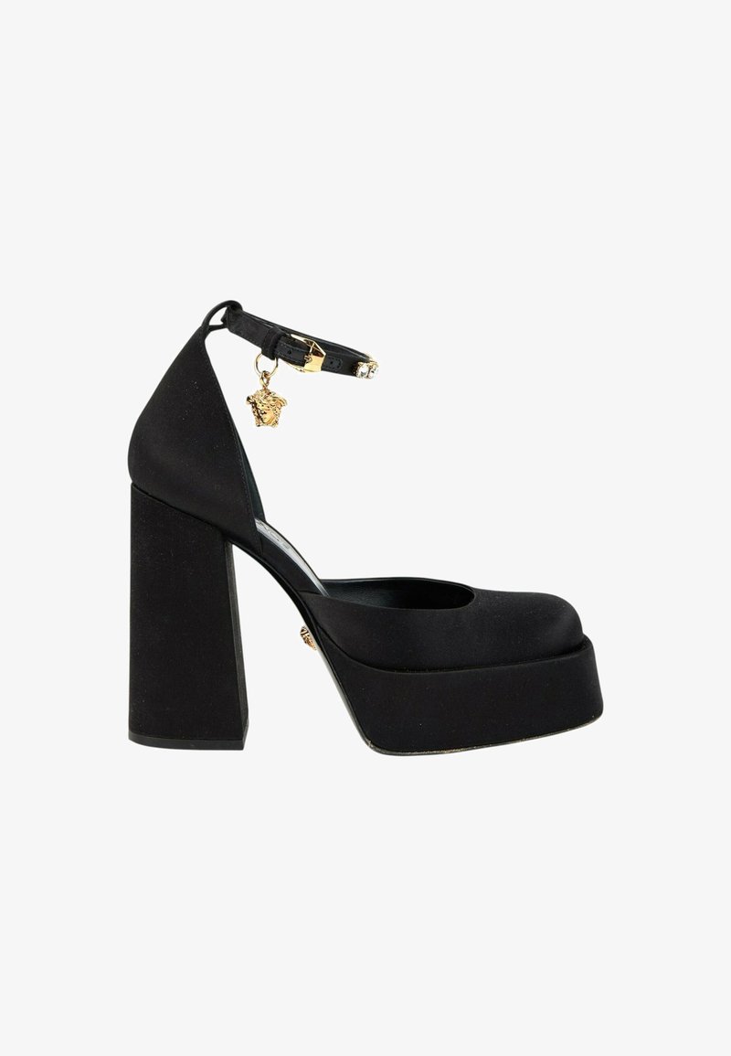 Chaussure à talon haut plateforme noire avec talon bloc épais, bride à la cheville et breloque tête de Méduse dorée sur la boucle de la bride.