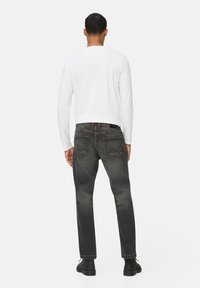 Ciemnoniebieskie dżinsy o prostym kroju, z dwiema tylnymi kieszeniami i delikatnym przetarciem. W zestawieniu z gładką, białą koszulą z długim rękawem.