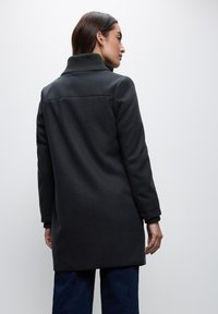 Schwarzer Wollmischmantel mit hoch gerafftem Kragen, langen Ärmeln und geradem Schnitt. Der Stoff hat eine weiche Textur und minimale Nähte.