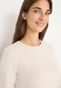 Pull léger beige à col rond, texture douce et motif subtil. Coupe près du corps avec un design minimal.