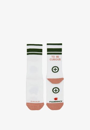 Calzini bianchi con strisce verdi, dettagli rosa e testo "TO BE CURIOUS." Presentano disegni circolari e marchio sulla suola.