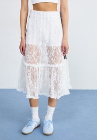 White lace midi skirt featuring a layered design, sheer panels, and scalloped hem. Paired with light blue sneakers and white socks.