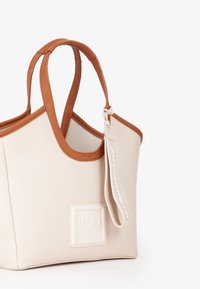 Borsa in pelle beige texturizzata con dettagli in pelle marrone; presenta manici corti e un'etichetta bianca con la scritta "IO SONO UNA BORSA RESPONSABILE."