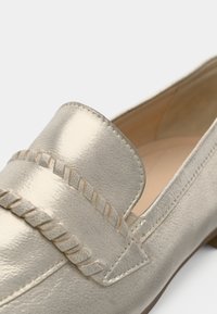 Metallik hõbedane loafer, sileda nahkpinnaga, millel on tuttidega aktsent ja tikandiga detailid peal. Madala kontsaga disain.