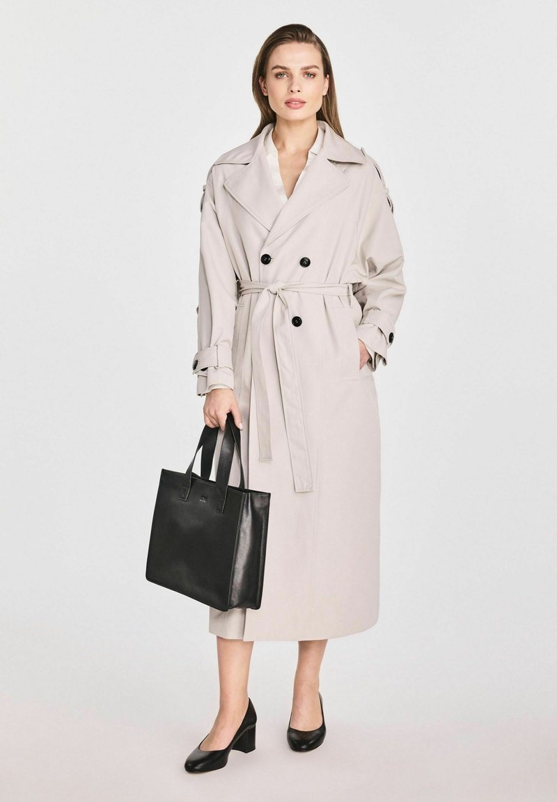 Jasny beżowy trencz o podwójnym zapięciu, z czarnymi guzikami i paskiem. Połączony z czarną skórzaną torebką oraz czarnymi obcasami na słupku.