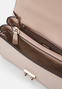 Ljusrosa handväska med slät yta, guldfärgade detaljer och flera fack, inklusive en zippered sektion och en märkesinredning.