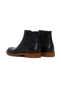 Bottines Chelsea en cuir noir avec panneaux latéraux élastiques, dos texturé, bout rond et talon en bois. Fini lisse avec des détails contrastants.