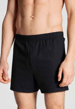 Boxers en coton noir avec une taille élastique, dotés d'une fermeture à bouton et d'une texture lisse. Conçus pour un design ajusté.