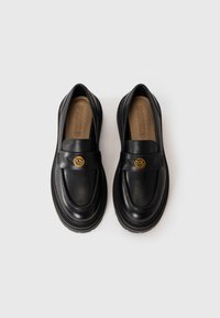 Black leather loafers with a rounded toe, smooth texture, thick sole, and a gold-tone logo accent on the front strap. Brand "PINKO" visible inside.