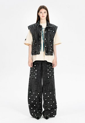 Joven mujer con chaqueta vaquera sin mangas gris lavado ácido y pantalones anchos con lunares blancos sobre una camiseta oversize crema.