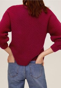 Jagodowy dzianinowy sweter z teksturowanym wzorem, szerokimi rękawami i zakrzywionym dołem, zestawiony z niebieskimi dżinsami z tylnymi kieszeniami.