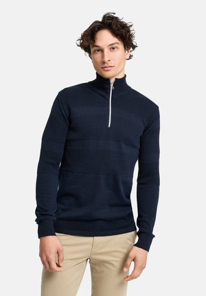 Marineblå halv-zip sweater med teksturerede mønstre, lange ærmer og ribbede krave. Har en kontrasterende sølvlynlås og subtile vandrette striber.