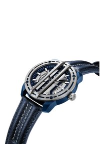 Ura z modrim usnjenim trakom, ki ima srebrno okroglo ohišje, teksturirano številčnico, izrazite kazalce ur in industrijske oblikovne poudarke.