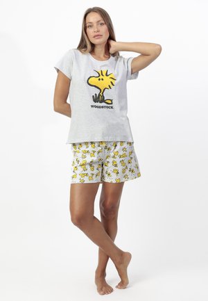 Mujer de pie descalza con camiseta gris con el personaje de Woodstock y pantalones cortos blancos a juego con estampados amarillos de Woodstock.
